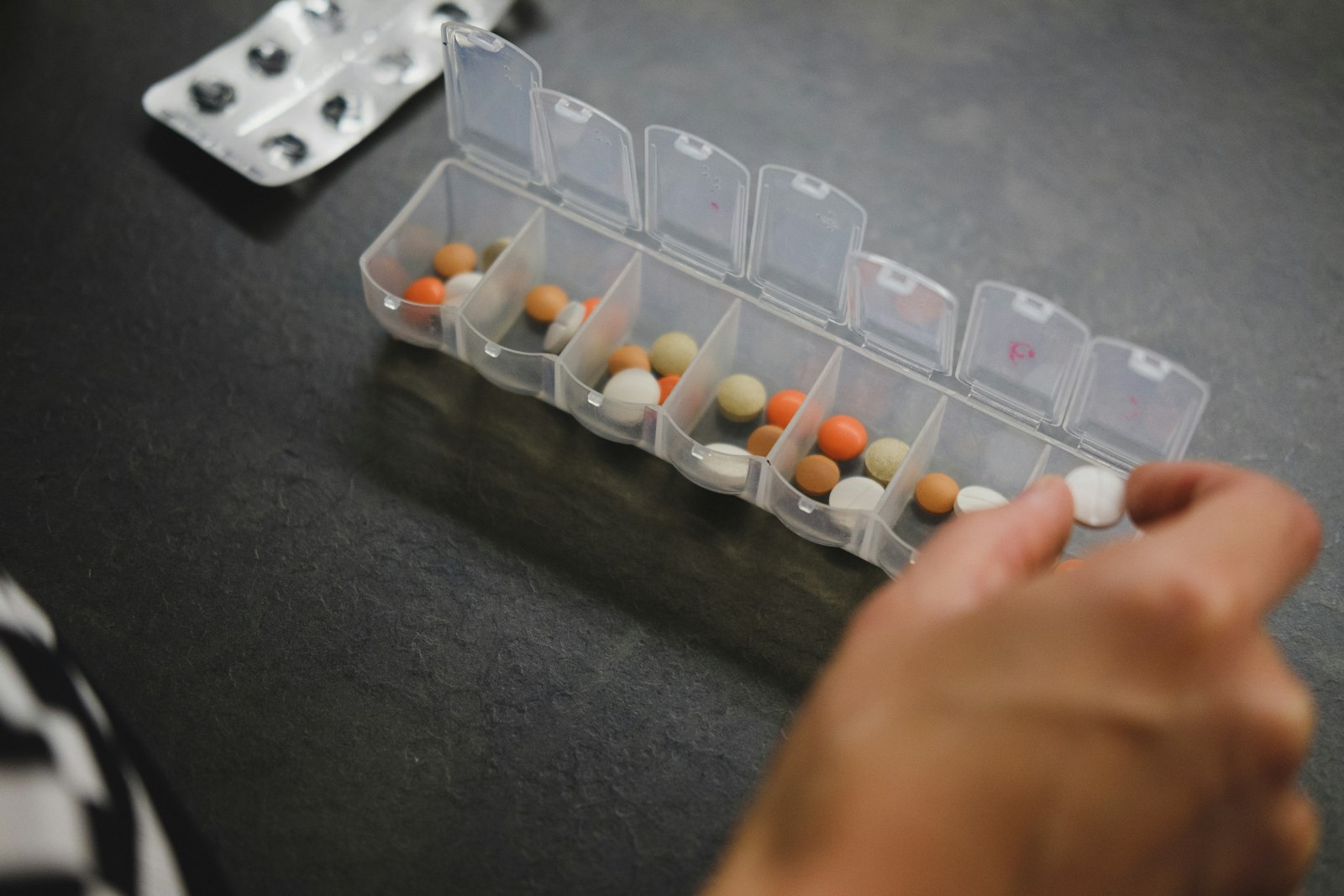 A weekly pill organizer being filled by hand